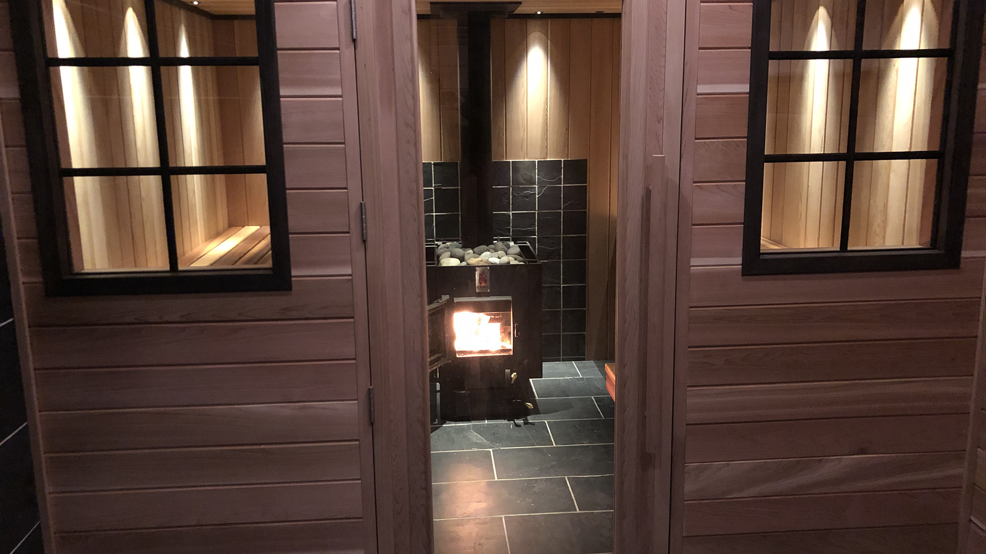 As you look through the glass door main entrance of the Imogene's Sauna you can see the warm glow of the sauna's fire.